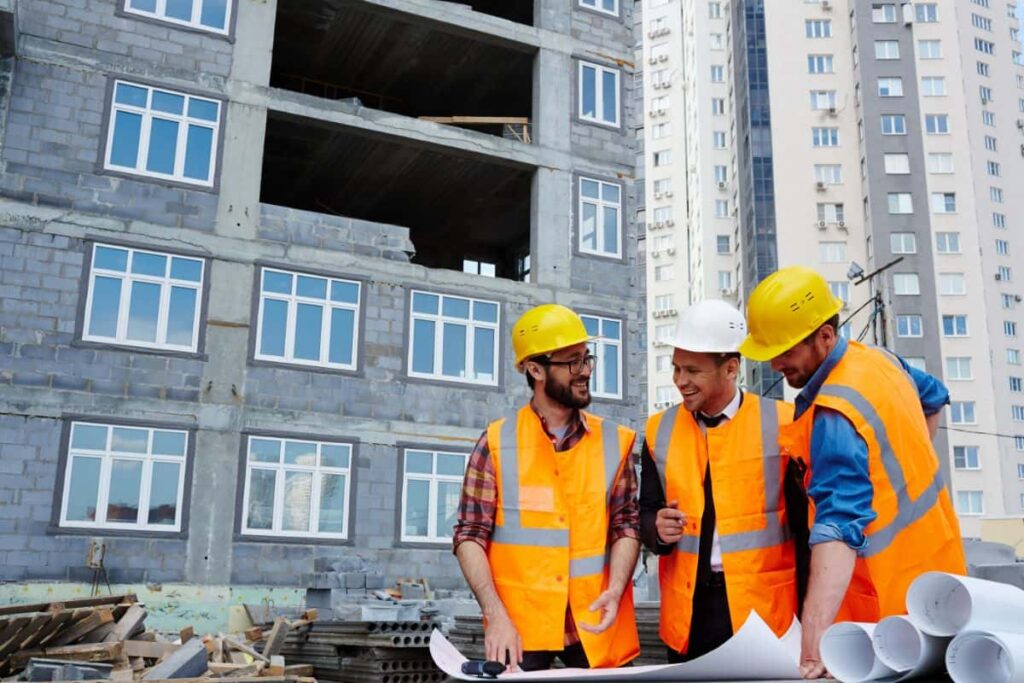 Group of construction workers in safety vests and helmets discussing building maintenance plans at a construction site.